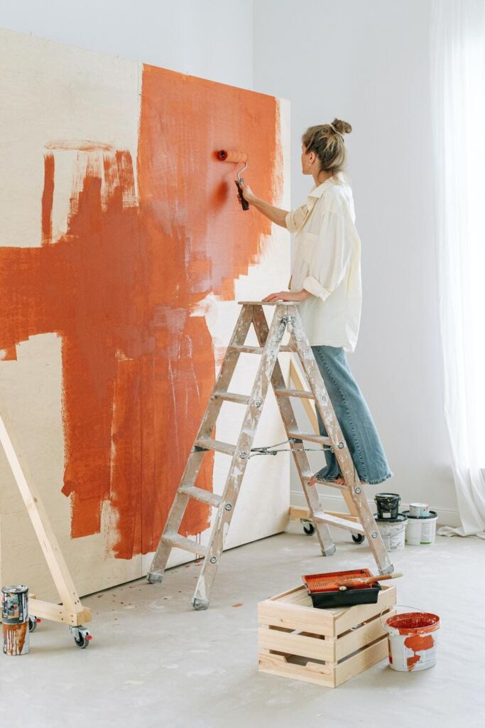Fille sur une échelle en train de peindre un mur de couleur orcre