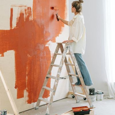 Fille sur une échelle en train de peindre un mur de couleur orcre
